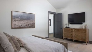 Een slaapkamer met een bed, een kaptafel, een televisietoestel en een schilderij aan de muur.