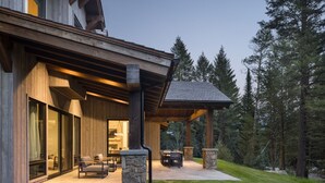 Een modern huis met een overdekt terras, stenen zuilen en uitzicht op het omliggende bos.