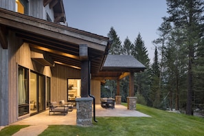 A modern house with a covered patio, stone pillars, and a view of the surrounding forest. - Luxury Private Mountain Home w/ Hot Tub (Jackson Hole)