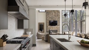 Een moderne keuken met een accentmuur van steen, een groot kookeiland en een eethoek met daglicht.