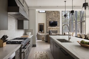 A modern kitchen with a stone accent wall, a large island, and a dining area with natural light. - Luxury Private Mountain Home w/ Hot Tub (Jackson Hole)