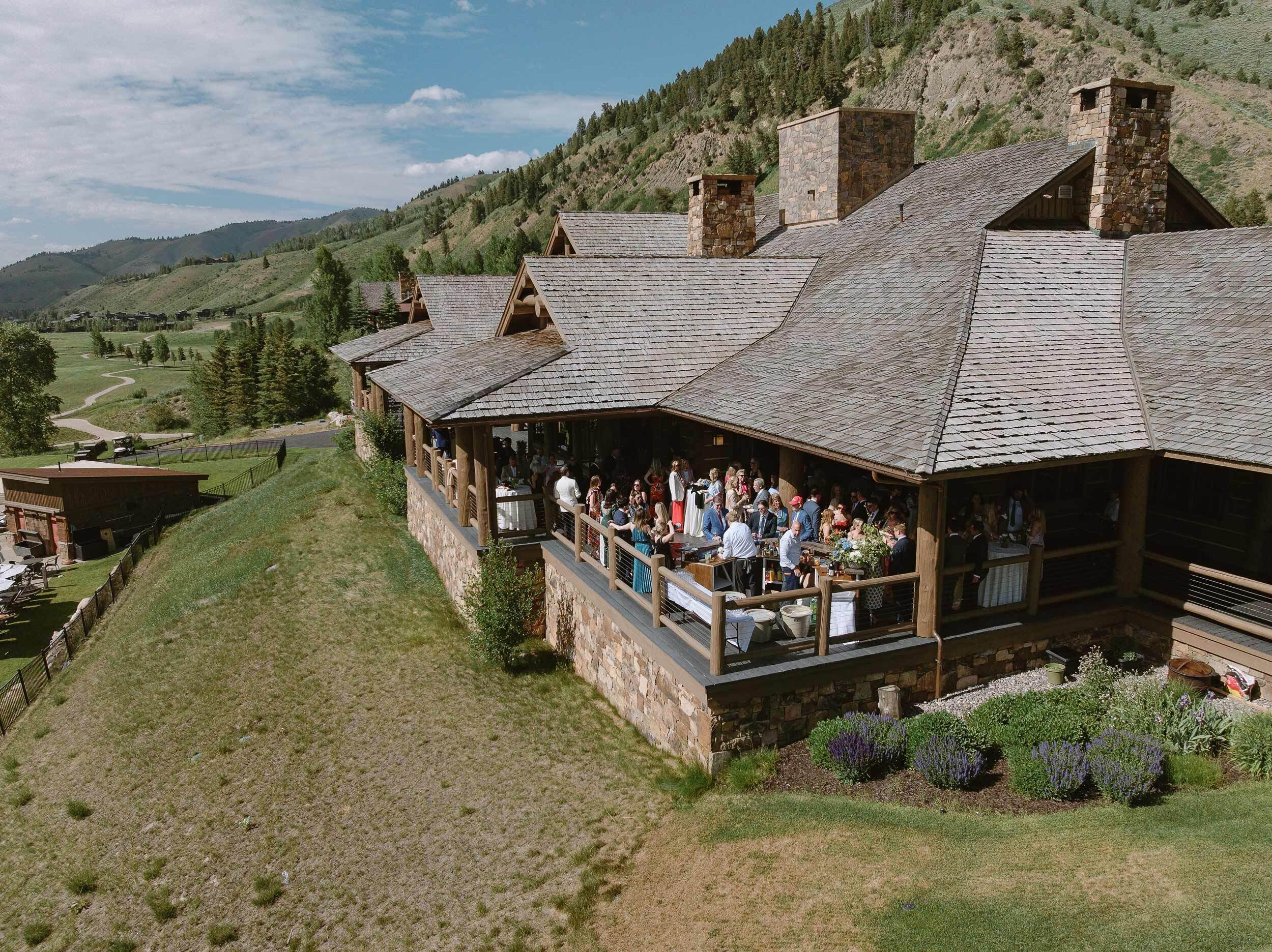 A lodge with a stone exterior, multiple chimneys, and a balcony area where guests are gathered.