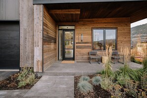 A modern building with a wooden exterior, a glass door, and a seating area with chairs and plants. - Elegant 4BR Meadow Cabin | Mountain View + Hot Tub (Jackson)
