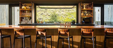 Un espace bar doté d’un long comptoir, de nombreux tabourets et d’étagères remplies de bouteilles et de verres.
