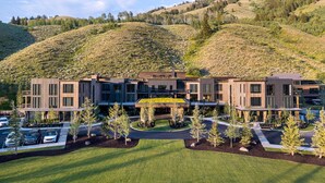 A modern multi-story building with a flat roof, surrounded by a well-maintained lawn and young trees. - Luxe 6BR Mountain Cabin w/ Premium Views & Hot Tub (Jackson)