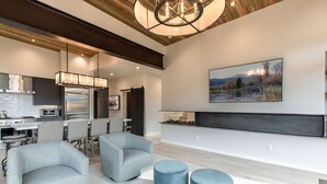 A modern living room with a fireplace, seating area, and kitchen in the background. - Luxe 6BR Mountain Cabin w/ Premium Views & Hot Tub (Jackson)