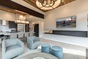 A modern living room with a fireplace, seating area, and kitchen in the background. - Luxe 6BR Mountain Cabin w/ Premium Views & Hot Tub (Jackson)