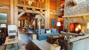 A log cabin interior with a stone fireplace, wooden furniture, and a cozy seating area. - Luxe 6BR Mountain Cabin w/ Premium Views & Hot Tub (Jackson)