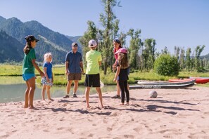 A group of people standing on a sandy beach with a calm body of water and mountains in the background. - Luxe 6BR Mountain Cabin w/ Premium Views & Hot Tub (Jackson)