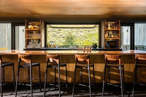 A bar area with a long counter, multiple stools, and shelves stocked with bottles and glasses.