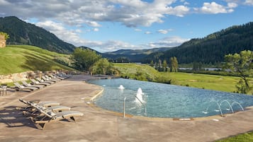 Une piscine dotée de chaises longues et d’une fontaine, le tout entouré d’un paysage montagneux.