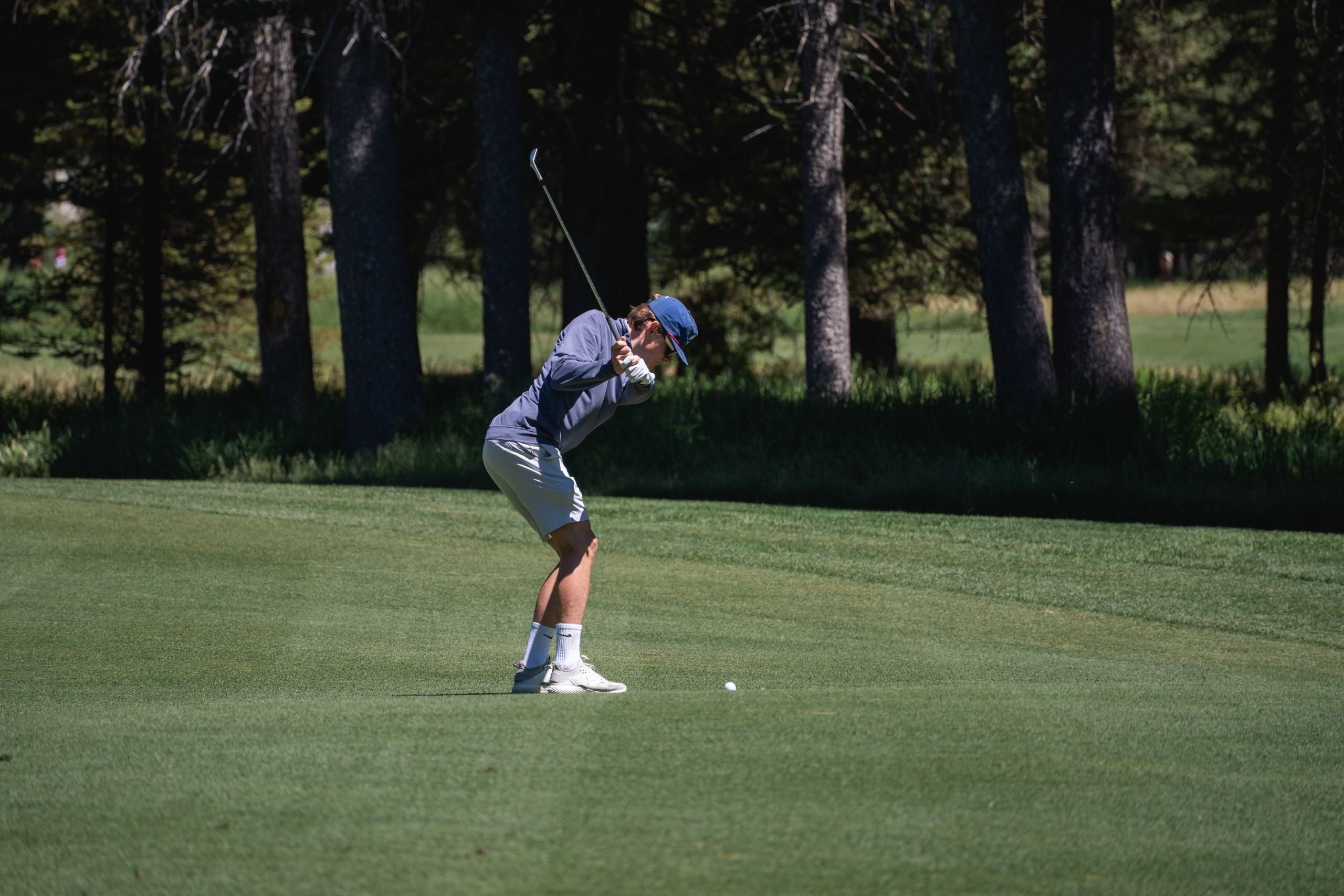 Une personne sur un terrain de golf, avec des arbres en arrière-plan.