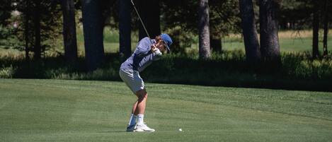 Una persona en un campo de golf, con árboles de fondo.