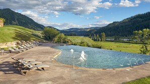 Una piscina con sillones de descanso y una fuente, rodeada por un paisaje montañoso.