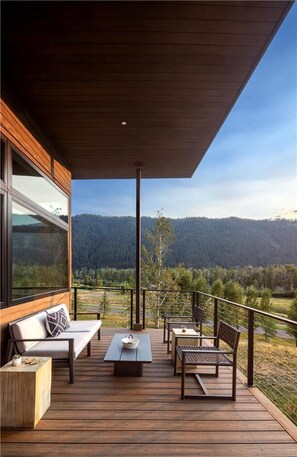 A wooden deck with outdoor furniture, a view of a forested mountain range, and a clear sky. - Serene 6BR Mountain Cabin | Premium View + Hot Tub (Jackson)