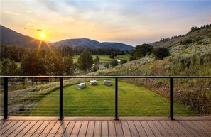 En træterrasse med udsigt over en græsplæne og fjerne bjerge.
