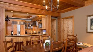 A wooden interior with a dining table, chairs, a chandelier, and a kitchen area. - Ski-In Condo | Tram-Adjacent | Mountain Views (Jackson Hole)