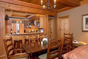 A wooden interior with a dining table, chairs, a chandelier, and a kitchen area. - Ski-In Condo | Tram-Adjacent | Mountain Views (Jackson Hole)