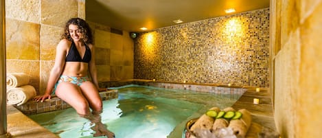 A person in a spa pool with a tiled wall and a bowl of fruits.