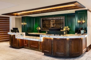 A reception desk with a marble top, wooden paneling, and a large framed artwork above. - Ski-In Condo | Tram-Adjacent | Mountain Views (Jackson Hole)