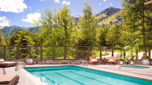 A swimming pool with a stone border, surrounded by lounge chairs and potted plants, with a mountain view in the background. - Ski-In Condo | Tram-Adjacent | Mountain Views (Jackson Hole)