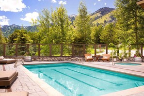 A swimming pool with a stone border, surrounded by lounge chairs and potted plants, with a mountain view in the background. - Ski-In Condo | Tram-Adjacent | Mountain Views (Jackson Hole)
