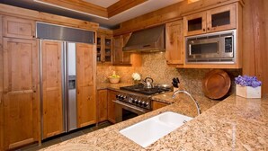 A kitchen with wooden cabinets, stainless steel appliances, granite countertops, and a built-in microwave. - Ski-In Condo | Tram-Adjacent | Mountain Views (Jackson Hole)