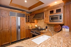 A kitchen with wooden cabinets, stainless steel appliances, granite countertops, and a built-in microwave. - Ski-In Condo | Tram-Adjacent | Mountain Views (Jackson Hole)