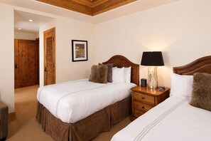Ein Hotelzimmer mit zwei Betten, Holz-Kopfteilen, einem Nachttisch mit Lampe, einem gerahmten Bild an der Wand und einer Holztür.