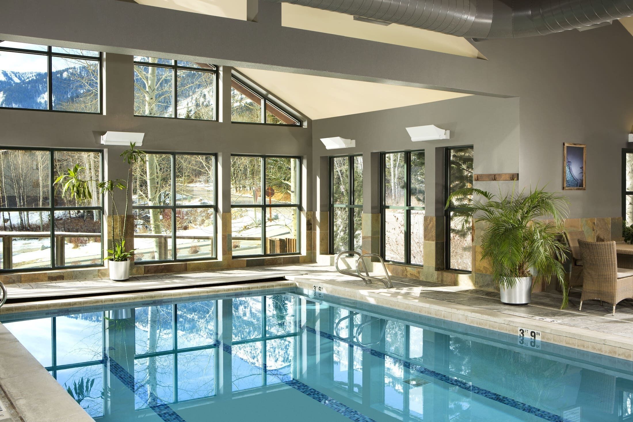 Une piscine intérieure dotée de grandes fenêtres, un espace détente avec des fauteuils et une vue sur un paysage enneigé.