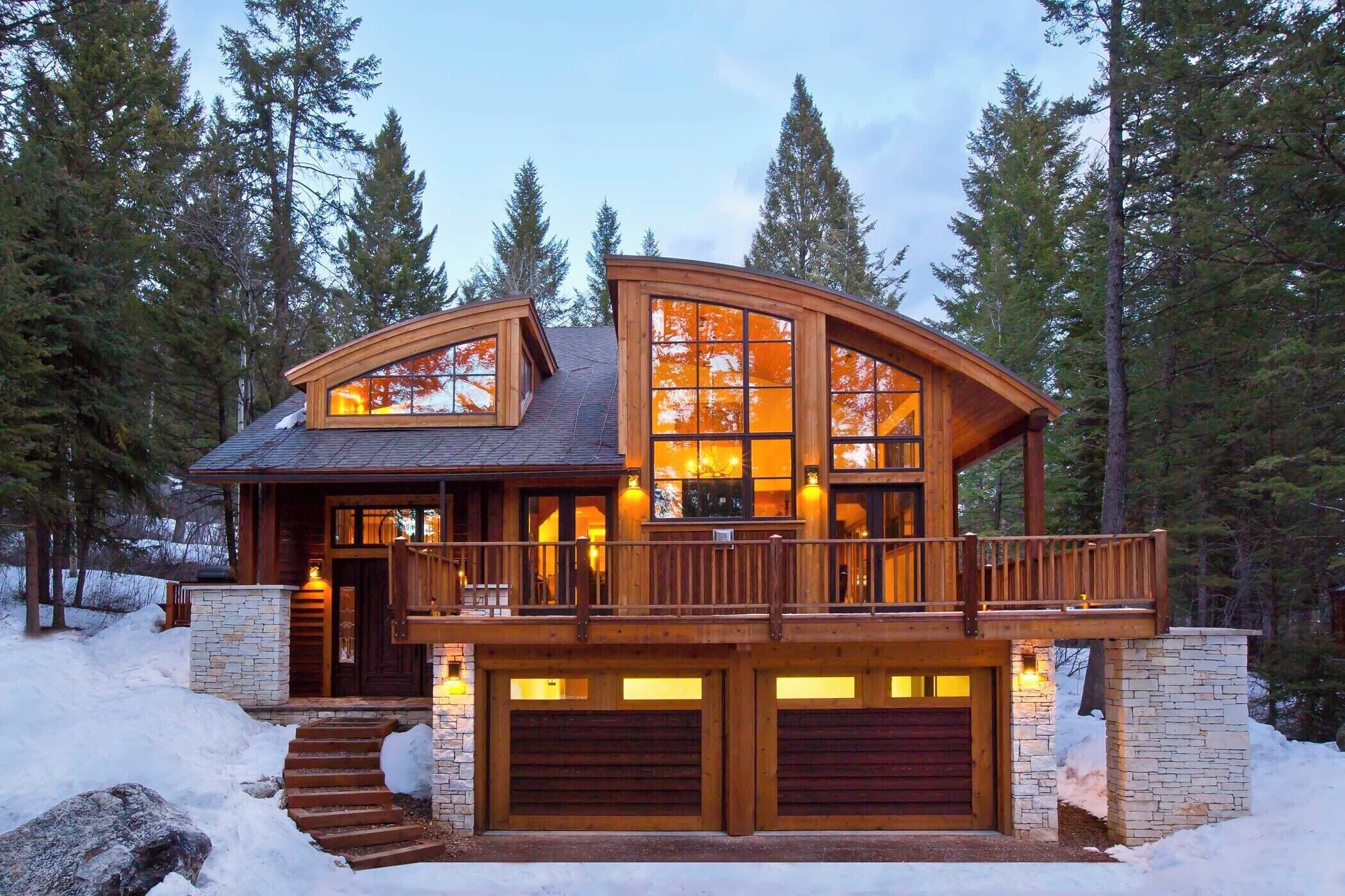 Une cabane en rondins à deux étages, dotée d’un balcon, de fondations en pierre et de grandes fenêtres.