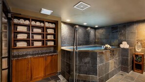 A modern bathroom with a built-in shower, a wooden towel rack, and a stone wall. - Grand Alpine Lodge w/ Sauna, Hot Tub & Game Room (Jackson Hole)