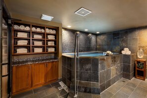 A modern bathroom with a built-in shower, a wooden towel rack, and a stone wall. - Grand Alpine Lodge w/ Sauna, Hot Tub & Game Room (Jackson Hole)