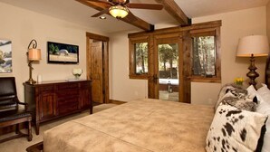 A bedroom with a large bed, wooden headboard, a ceiling fan, a wooden dresser, a television, and a window with a view of trees. - Grand Alpine Lodge w/ Sauna, Hot Tub & Game Room (Jackson Hole)