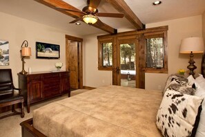 A bedroom with a large bed, wooden headboard, a ceiling fan, a wooden dresser, a television, and a window with a view of trees. - Grand Alpine Lodge w/ Sauna, Hot Tub & Game Room (Jackson Hole)