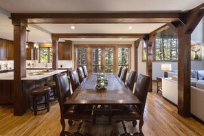 Une salle à manger spacieuse, avec une longue table en bois, des chaises en cuir et une vue sur la forêt grâce à de grandes fenêtres.