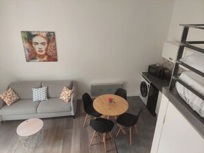 A compact living space with a sofa, a round dining table, and a small kitchen area. - Charming apartment just steps from the historic center and hiking trails (Le Puy-en-Velay)
