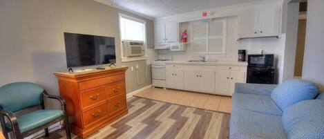 A compact living space with a kitchenette, a sofa, a television, and a wooden cabinet.