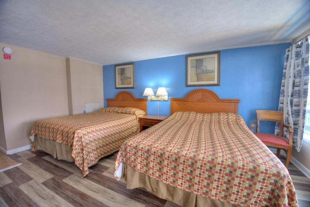 Habitación de hotel con dos camas individuales, una mesita de noche con lámparas, una silla y una ventana con cortinas.