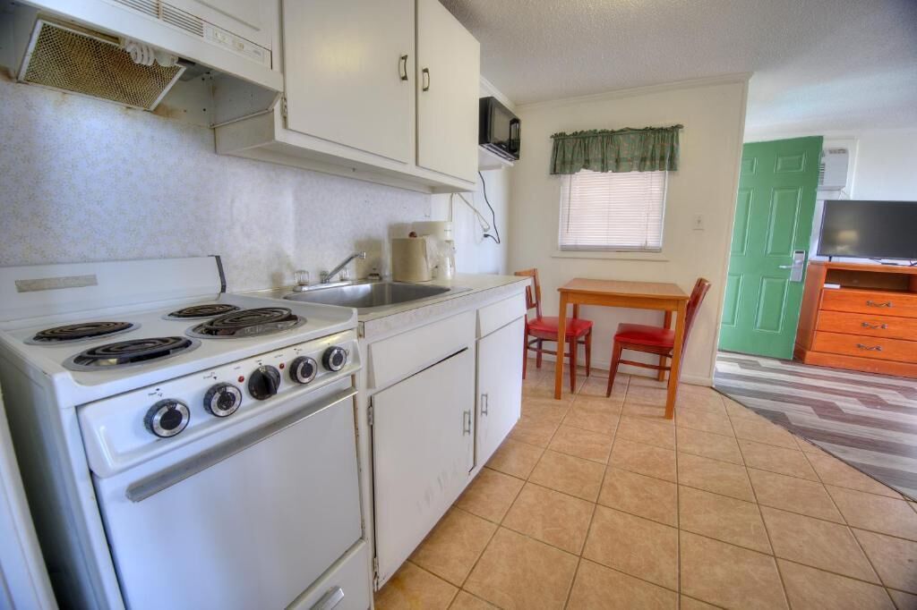 Cocina compacta con estufa, lavamanos y comedor con mesa y sillas.