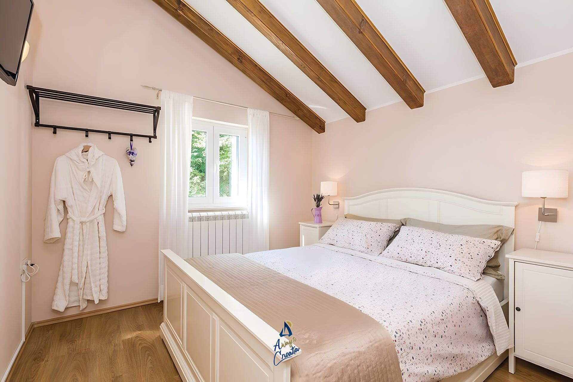 Una camera da letto con un letto, comodini, una finestra e un accappatoio appeso a un appendiabiti.