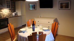 En matplats med ett runt bord för två personer, ett vitt skåp och en tv som är monterad på väggen.