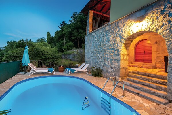 Una piscina con sillas de descanso y un muro de piedra con una puerta roja.