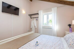 Ein Schlafzimmer mit einem Bett, einem an der Wand montierten Fernseher, einem Fenster mit Vorhängen und einer Heizung.