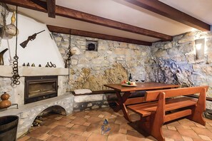 Ein rustikaler Innenraum aus Stein mit Kamin, Holzbalken und einer Steinsitzbank.