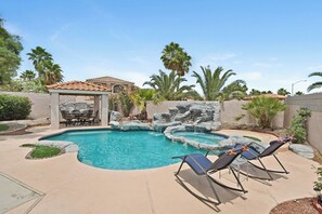A backyard with a swimming pool, lounge chairs, a covered patio, and a rock waterfall feature. - Cozy 3-bedroom home in beautiful Henderson with cool pool (Henderson)