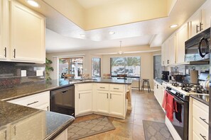 A modern kitchen with white cabinets, a granite countertop, a central island, and a gas stove. - Cozy 3-bedroom home in beautiful Henderson with cool pool (Henderson)