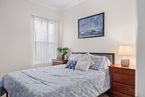 A bedroom with a bed, a nightstand, a lamp, a window with curtains, and a painting on the wall. - Reunion Relaxation - Disney/South Pool/Outdoor TV (Kissimmee)