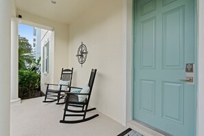 A porch with two rocking chairs, a wall-mounted compass, and a teal door with a keypad lock. - Reunion Relaxation - Disney/South Pool/Outdoor TV (Kissimmee)
