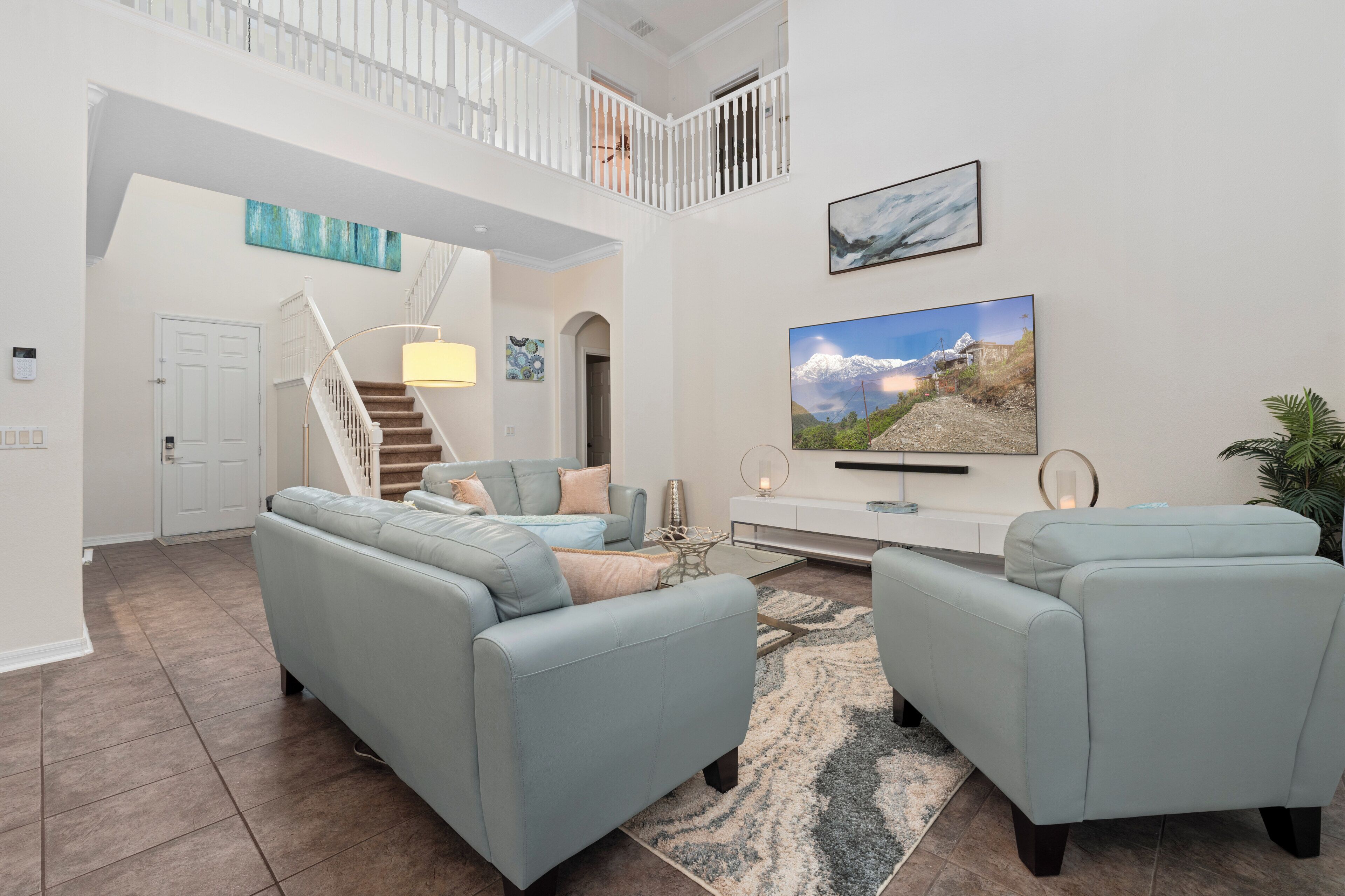 A spacious living room with a high ceiling, a staircase, and a large window.